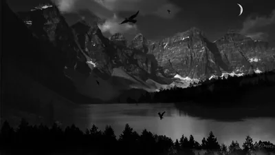 Birds cross a monochrome valley where snow-streaked peaks drop into still water, a thin crescent moon hanging in the upper right.