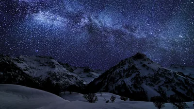 Thousands of stars and a faint Milky Way band stretch over moonlit snow slopes, deep navy tones sitting comfortably behind white app icons.