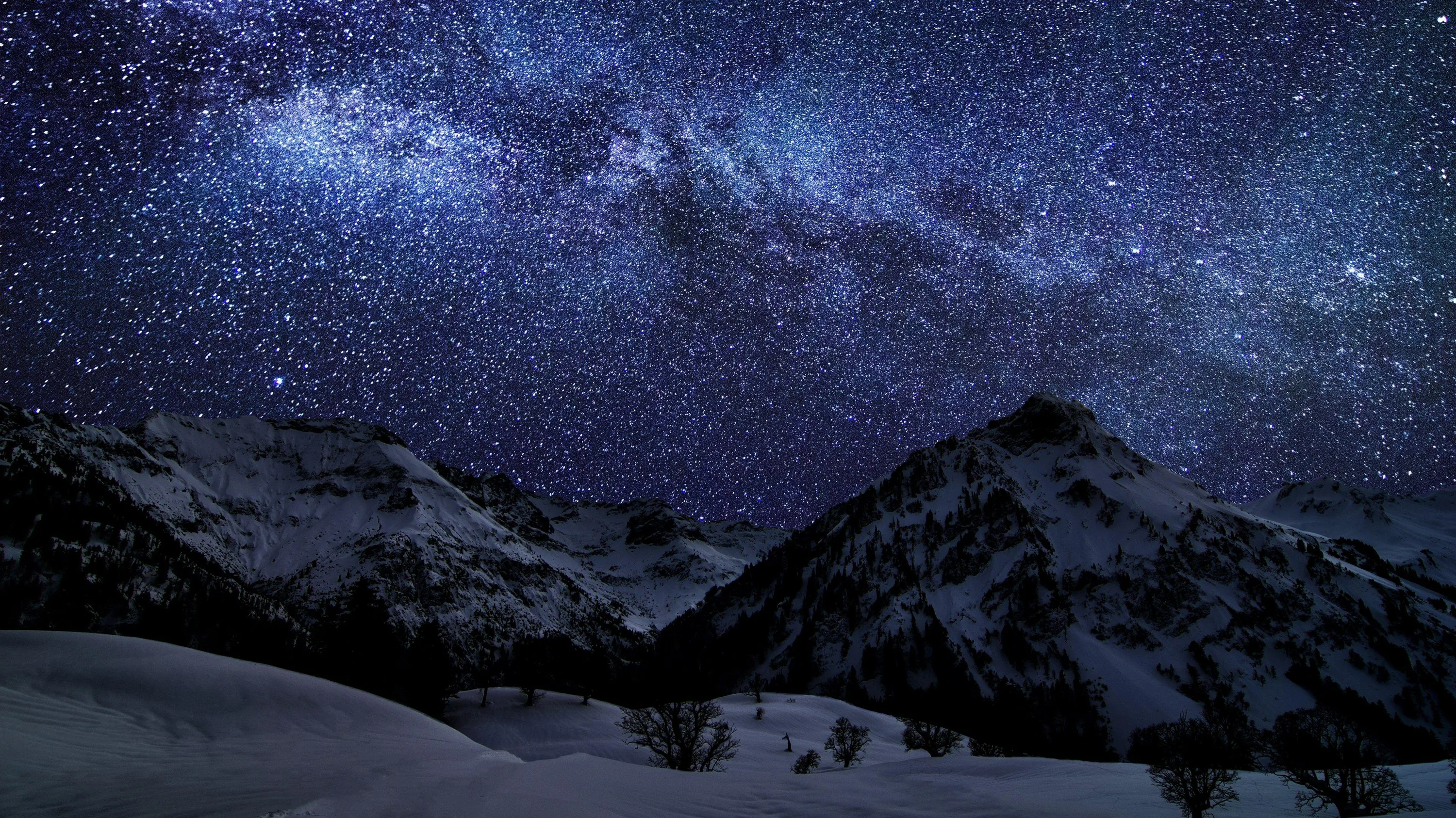 Thousands of stars and a faint Milky Way band stretch over moonlit snow slopes, deep navy tones sitting comfortably behind white app icons.