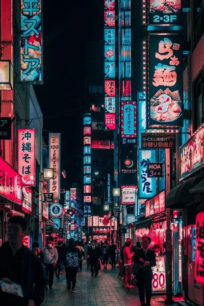 Cyan and magenta signs, one carrying a ramen shop mascot, crowd both sides of a night alley with a thin dark sky sliver at top.