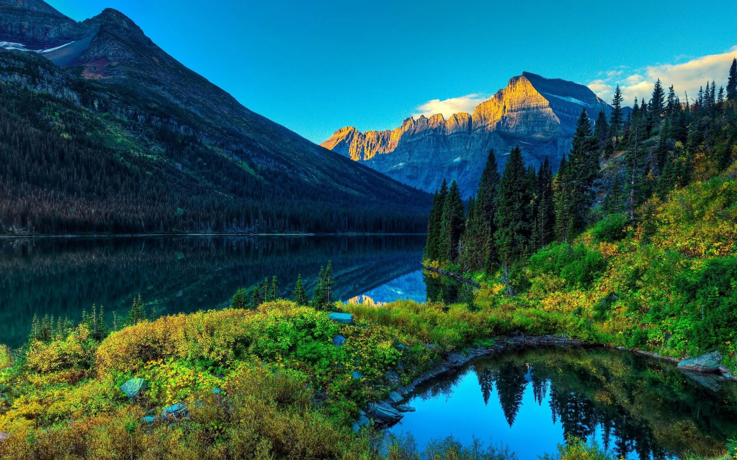 First light hits only the far peak while the valley stays in shadow; a round pond in the foreground repeats the mountain in miniature at bottom right.