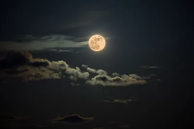 An amber moon hangs above a low shelf of dimly lit clouds, most of the frame kept near-black so the warm disc carries all the light.