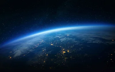 Earth's night side curves across the frame under a faint blue atmospheric arc, scattered city lights in the centre leaving both upper corners fully dark.