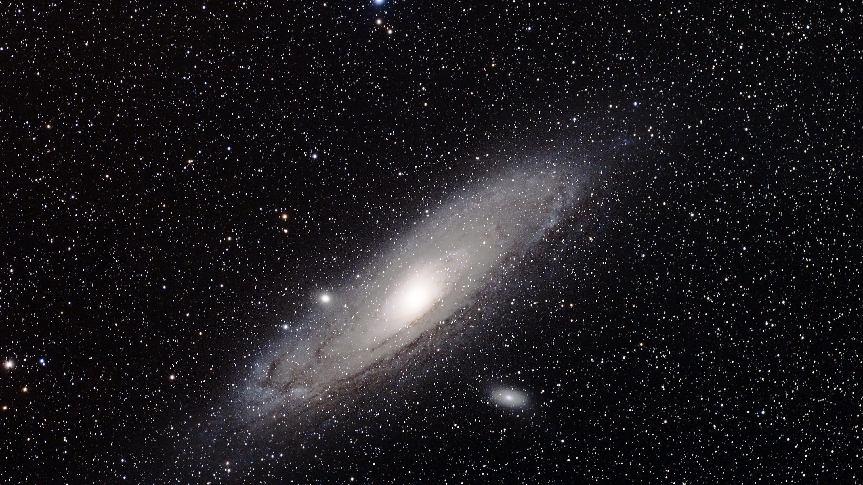A large tilted galaxy sits left of centre in warm greyscale with two small companion galaxies nearby and stars spread thinly around it.