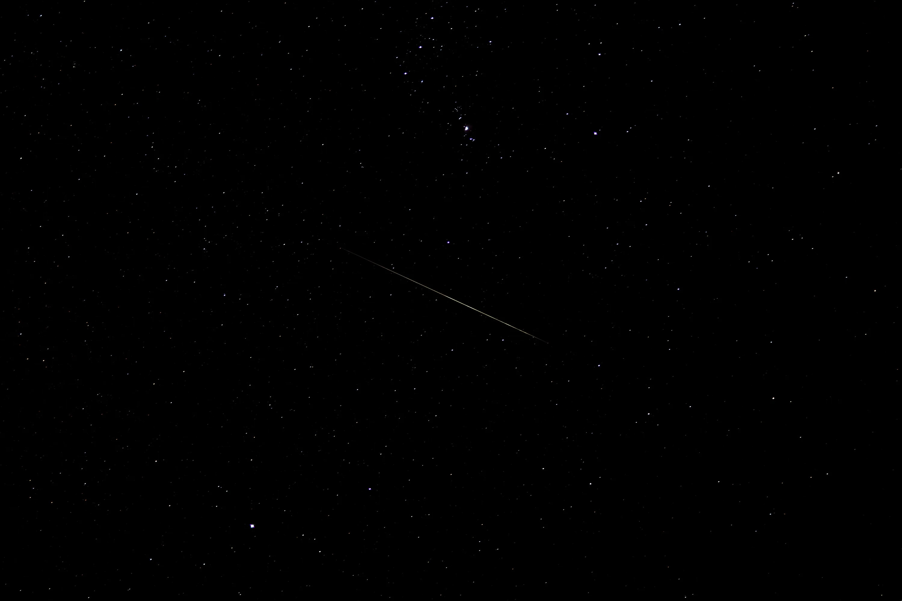 A short meteor trail crosses the middle of an otherwise quiet sky, the stars thin and the corners almost pure black.