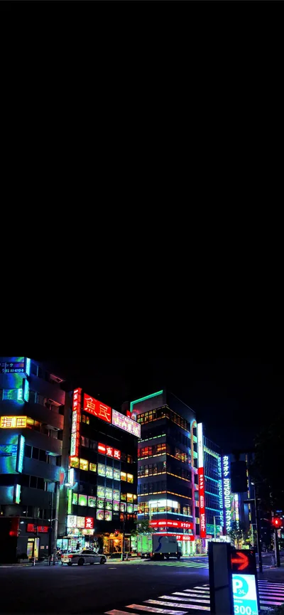 A street corner stacked with lit shopfront signs in red, blue and green, the sky above them dropping straight to black.