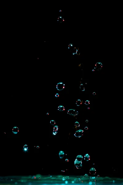 Teal-lit bubbles drift upward through black water, largest near the bottom and thinning out well before the top of the frame.