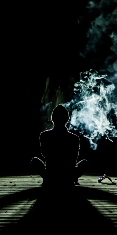 Backlight traces the outline of a person seated cross-legged while smoke curls off to the right, the top quarter of the frame pure black for a clock.