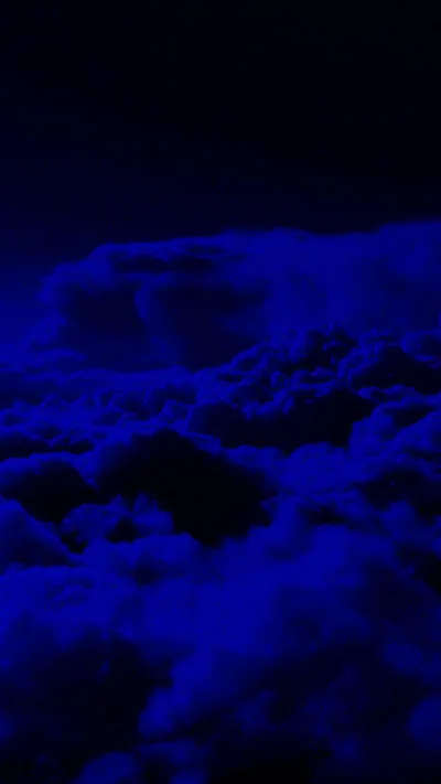 Banked clouds glow electric blue from below and pile up the vertical frame, the top third left almost fully black.
