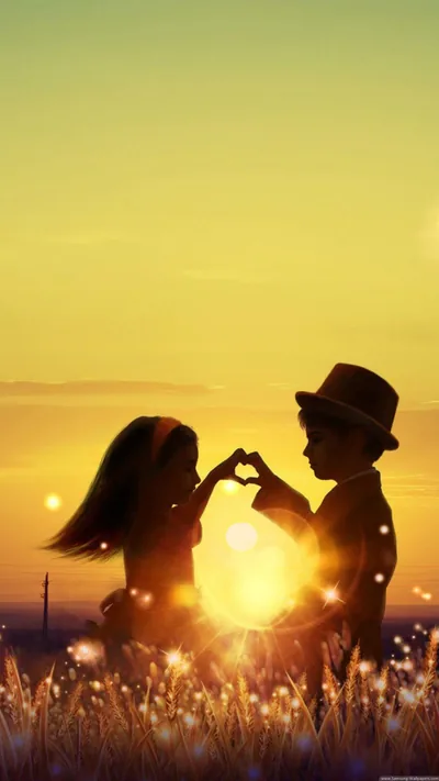 A boy in a hat and a girl press their hands into a heart in tall grass, the low sun burning through the gap between them.