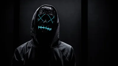 A figure in a black hoodie faces the camera, cyan stitched lines across the mask the only light in an otherwise grey-black frame.