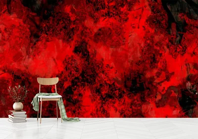 A wall of red and black ink marbling photographed behind a pale wooden chair and a small stack of books on a herringbone floor.