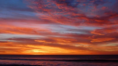 Layered bands of red, orange and violet cloud above a darkening ocean, the last glow pooling just left of centre on the horizon.