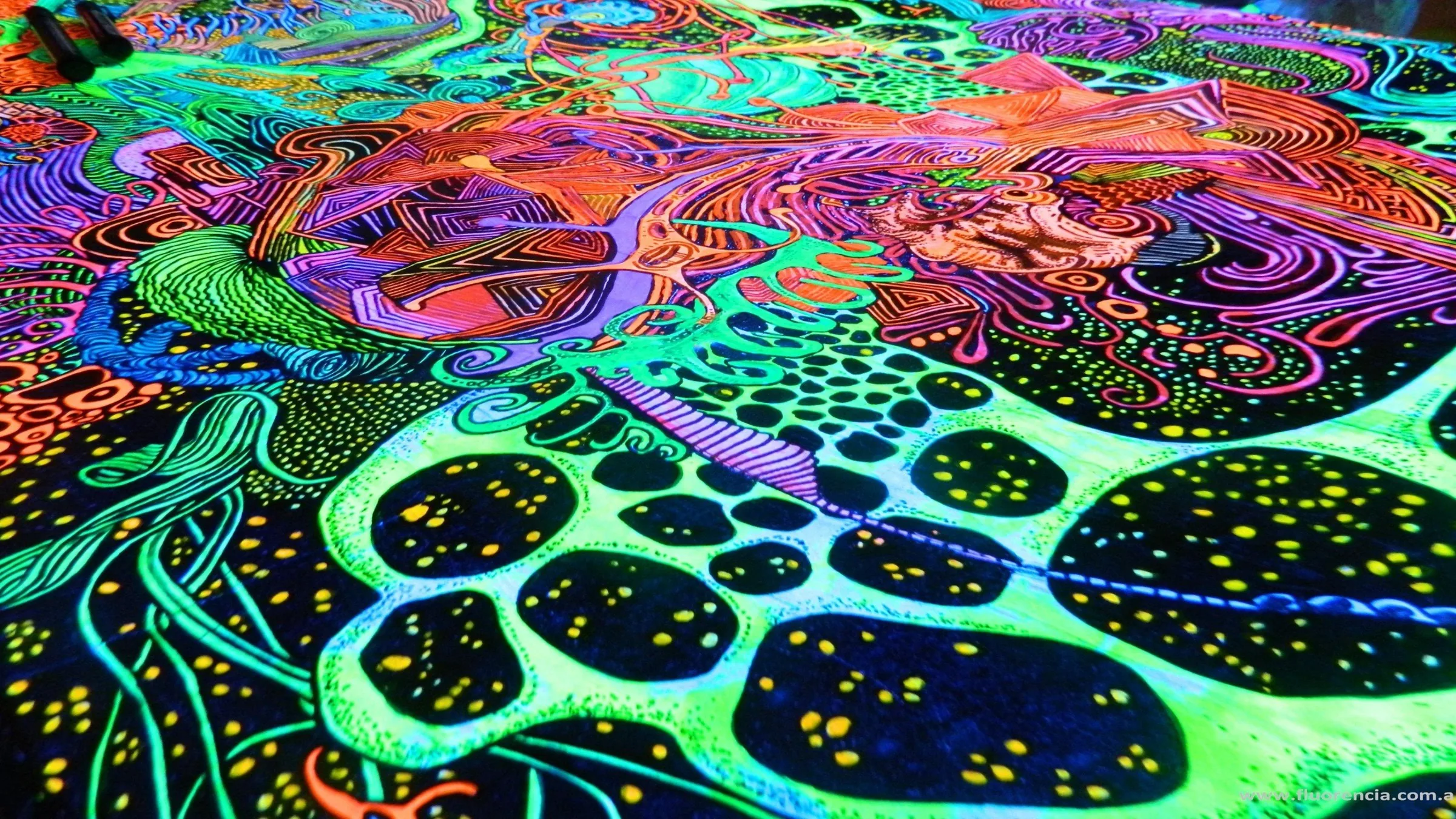 A UV-reactive painted surface shot at an angle, black cell shapes speckled with yellow floating over glowing green and pink linework.