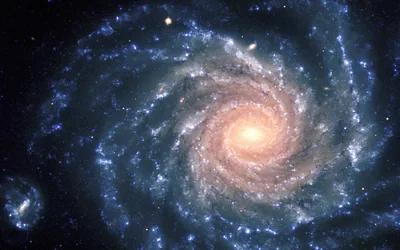 A face-on spiral seen from above, blue-white arms winding into a golden core that sits just right of centre against near-black space.