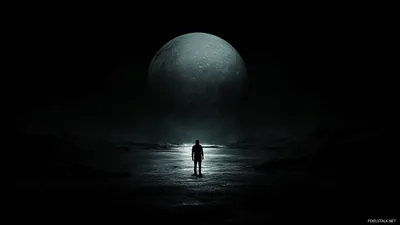 A lone silhouette stands on wet ground while an enormous moon fills the sky behind him.