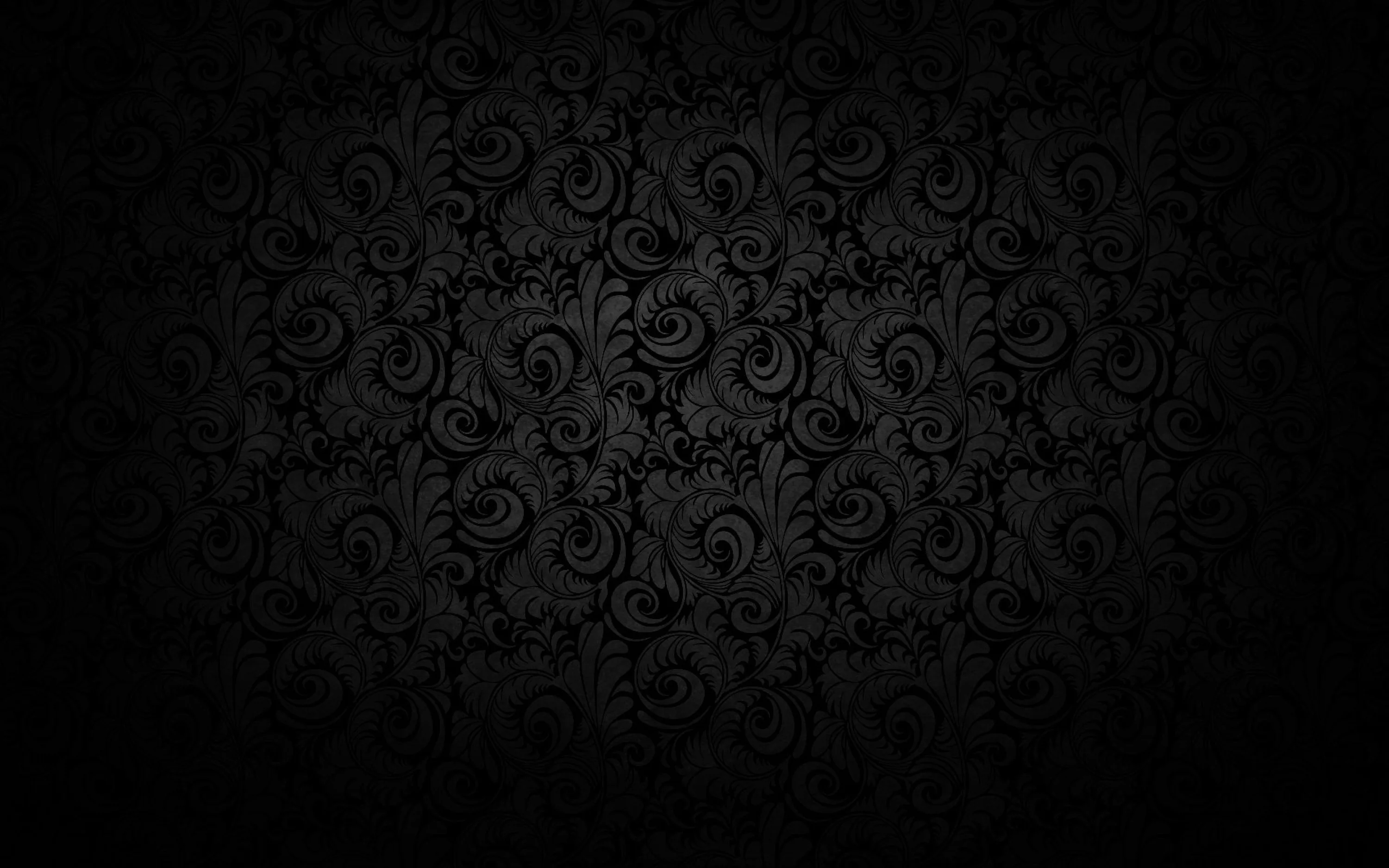 An ornate scroll pattern fills a charcoal wall, fading into full black at every corner of the frame.