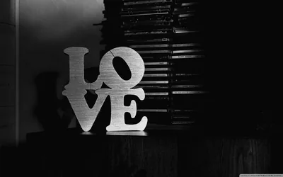 A stacked LOVE sculpture sits in front of a dark slatted wall, side light catching the grain in monochrome.