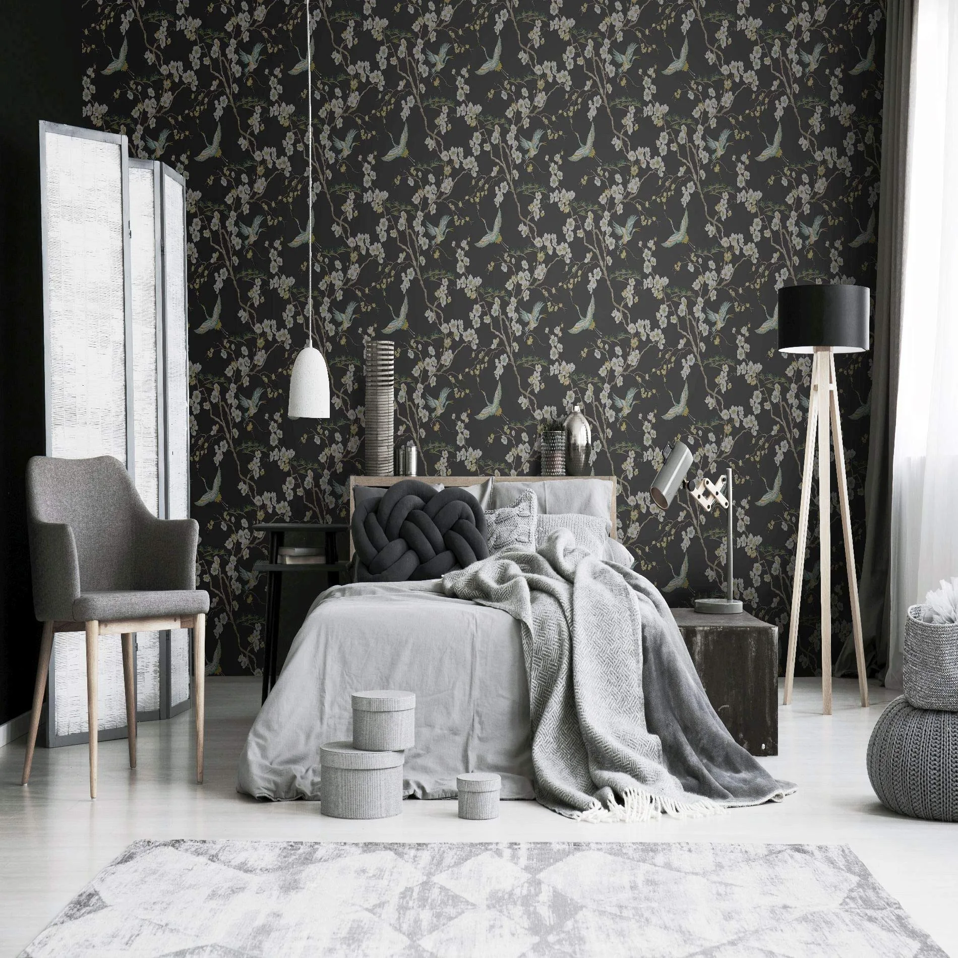 A styled bedroom with grey bedding sits against a black botanical mural wall; the white plank floor and rug hold the bottom third.