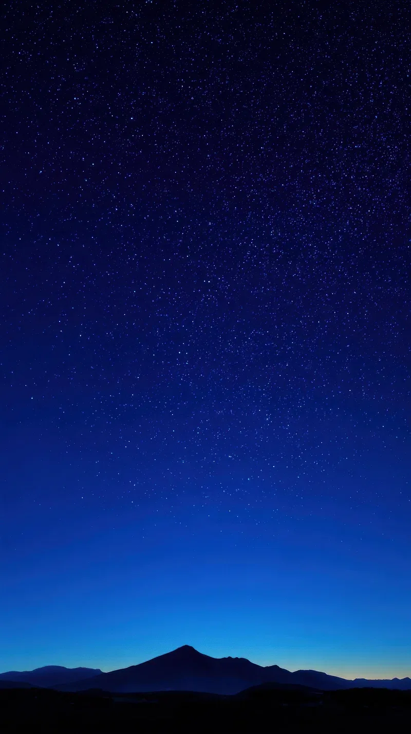 A cone-shaped peak sits low in the frame under a deep blue sky packed with stars, the horizon holding a last thin band of dusk light.