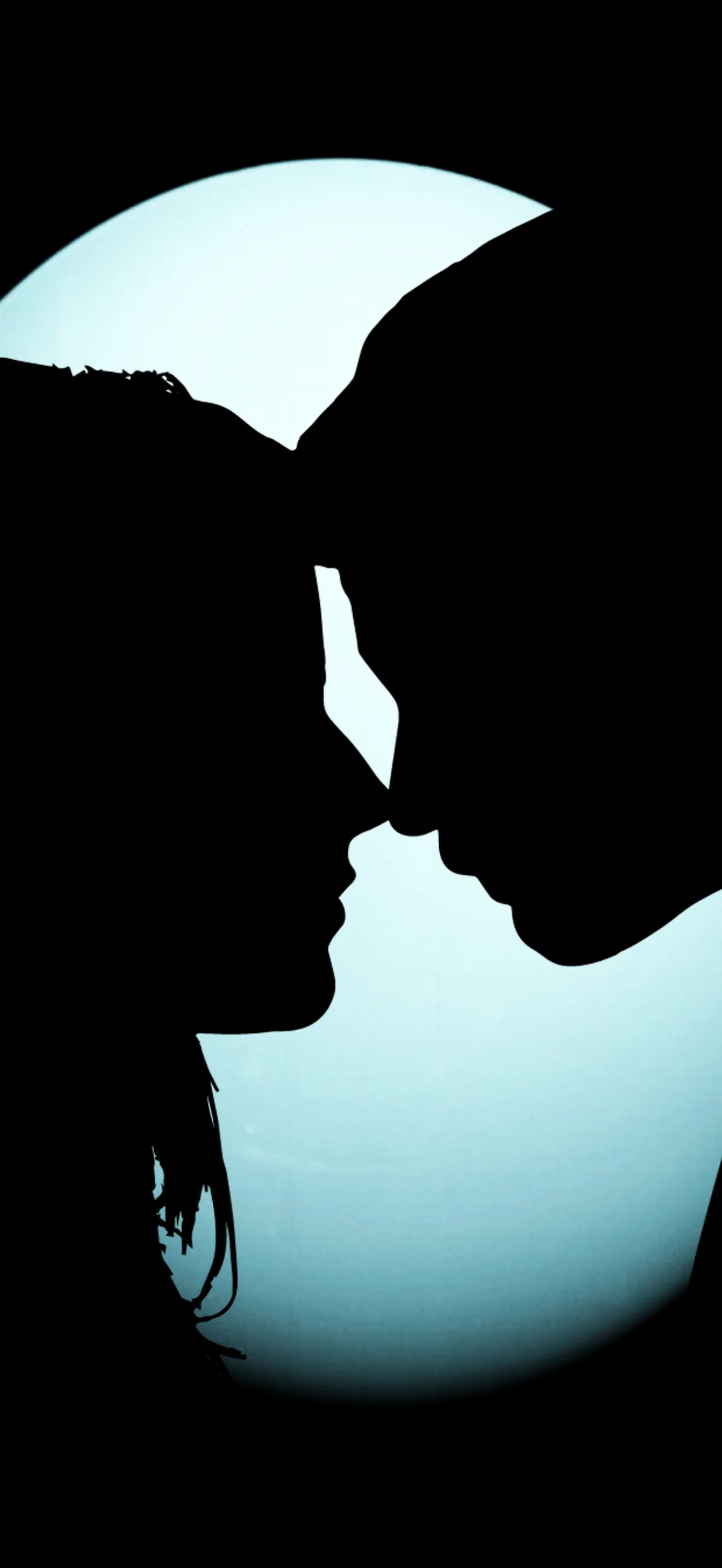 Two profiles cut in full black lean together in front of a pale moon disc, the tall frame leaving the top third empty.