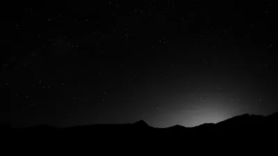 Stars fill the upper frame while a low glow sits behind a black ridge line along the bottom.