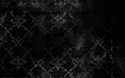A worn damask pattern shows through grime and scratches on a black wall, heaviest around the middle and lost entirely in the corners.