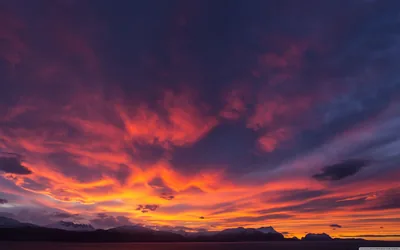 Red and violet cloud sweeps over a jagged mountain silhouette after sundown, the fire concentrated in a band across the middle of the frame.