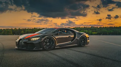 A black Chiron with a red centre stripe parked on open runway asphalt, treeline behind it and torn orange clouds filling the sky.