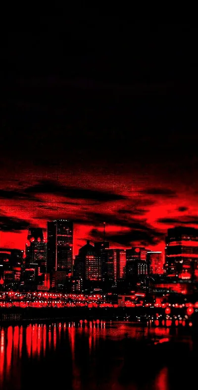 A skyline stands in silhouette under a sky processed to pure red and black, its lights repeating in the water below, the upper third almost fully dark.