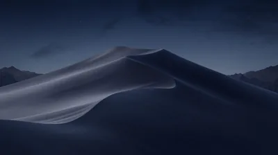 A single tall dune curves through cool blue darkness, its windward face lit while the ridges behind sink into shadow.
