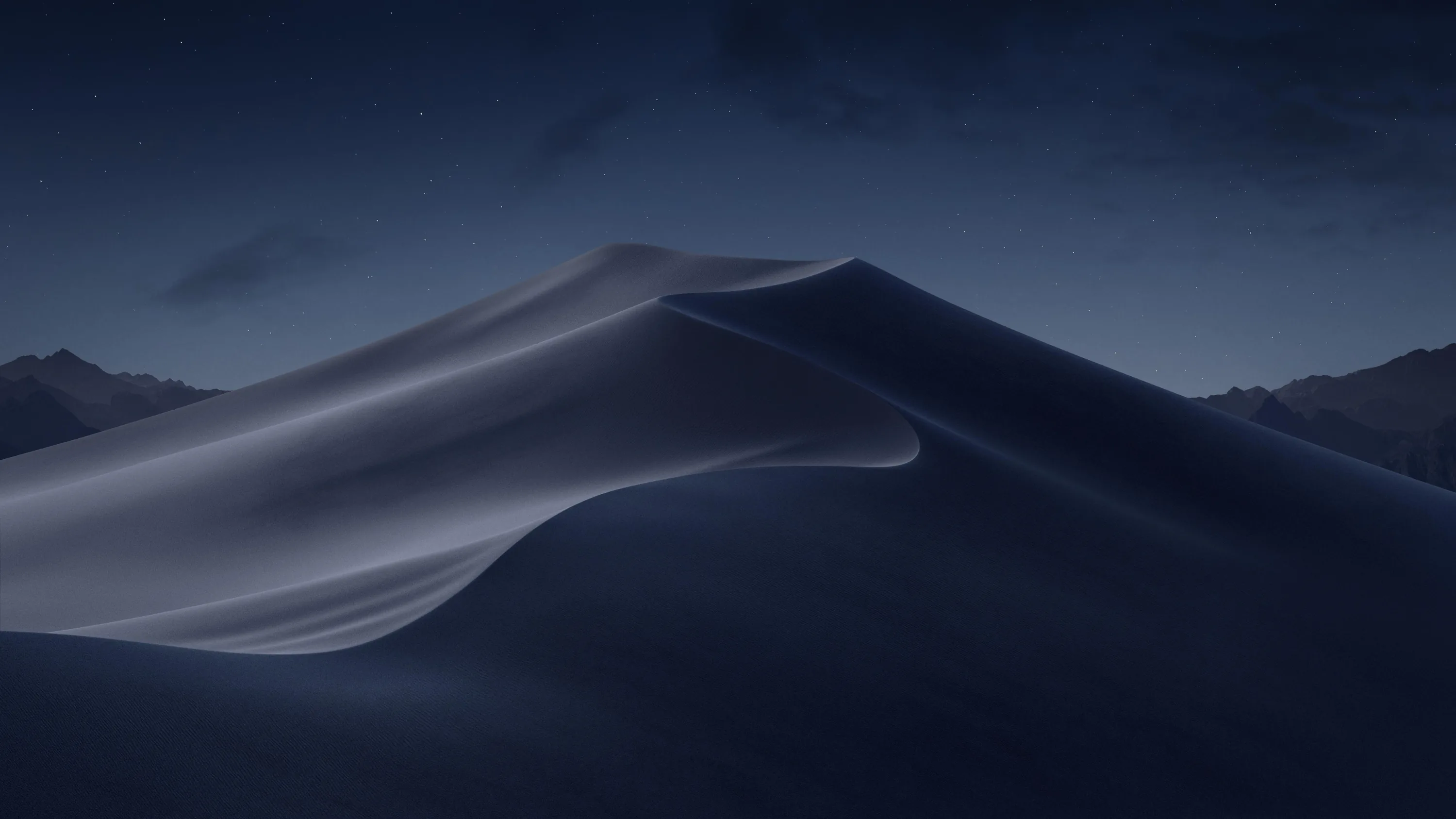 A single tall dune curves through cool blue darkness, its windward face lit while the ridges behind sink into shadow.