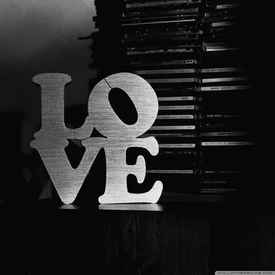 The word LOVE cut from pale board and stacked two letters over two, sitting in front of rows of disc cases in grainy black and white.