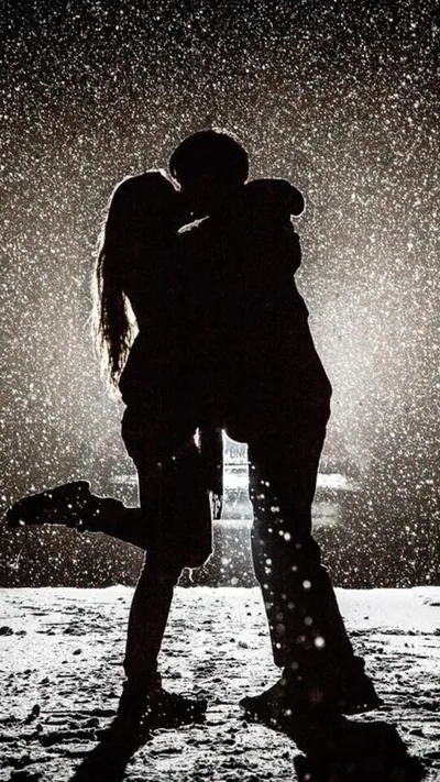 A couple kiss under falling rain, shot in black and white so the drops read as bright streaks against the dark street behind them.