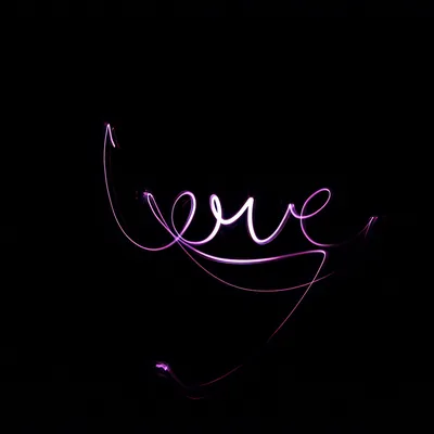 A long exposure traces the word love in violet light, the loops trailing off into faint curves at the bottom of an otherwise black frame.