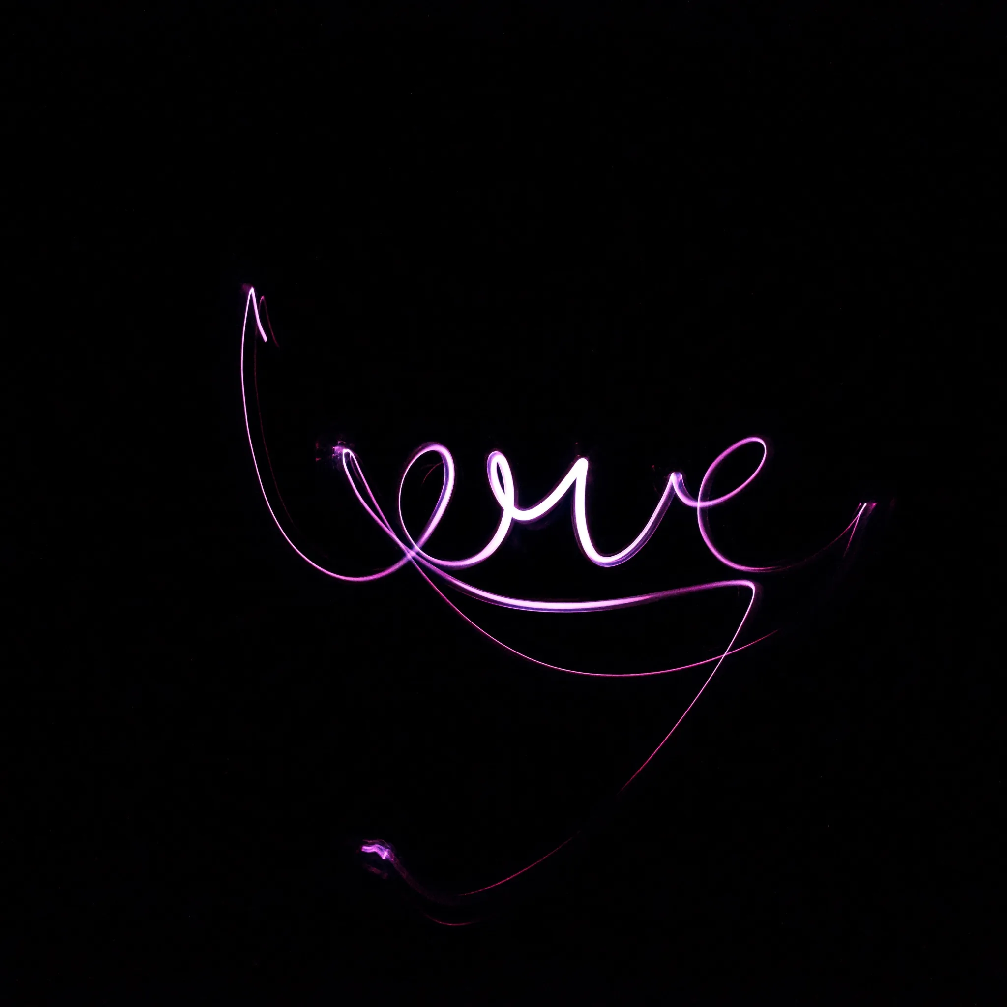 A long exposure traces the word love in violet light, the loops trailing off into faint curves at the bottom of an otherwise black frame.
