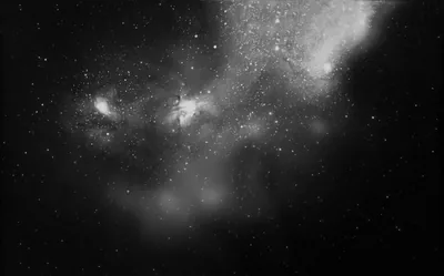A faint nebula spreads across the upper frame in soft grey, bright stars packed thickest near its centre.