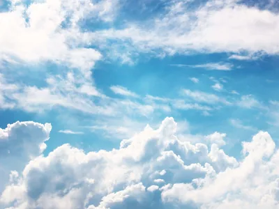 Sunlit cumulus piles up across the lower half under hazy summer light, leaving the top of the frame in open blue where a phone clock stays readable.