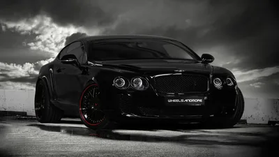 A stanced Continental GT shot low against dark cloud, its blacked-out mesh grille and quad headlamps sharp while red split rims sit under the arches.