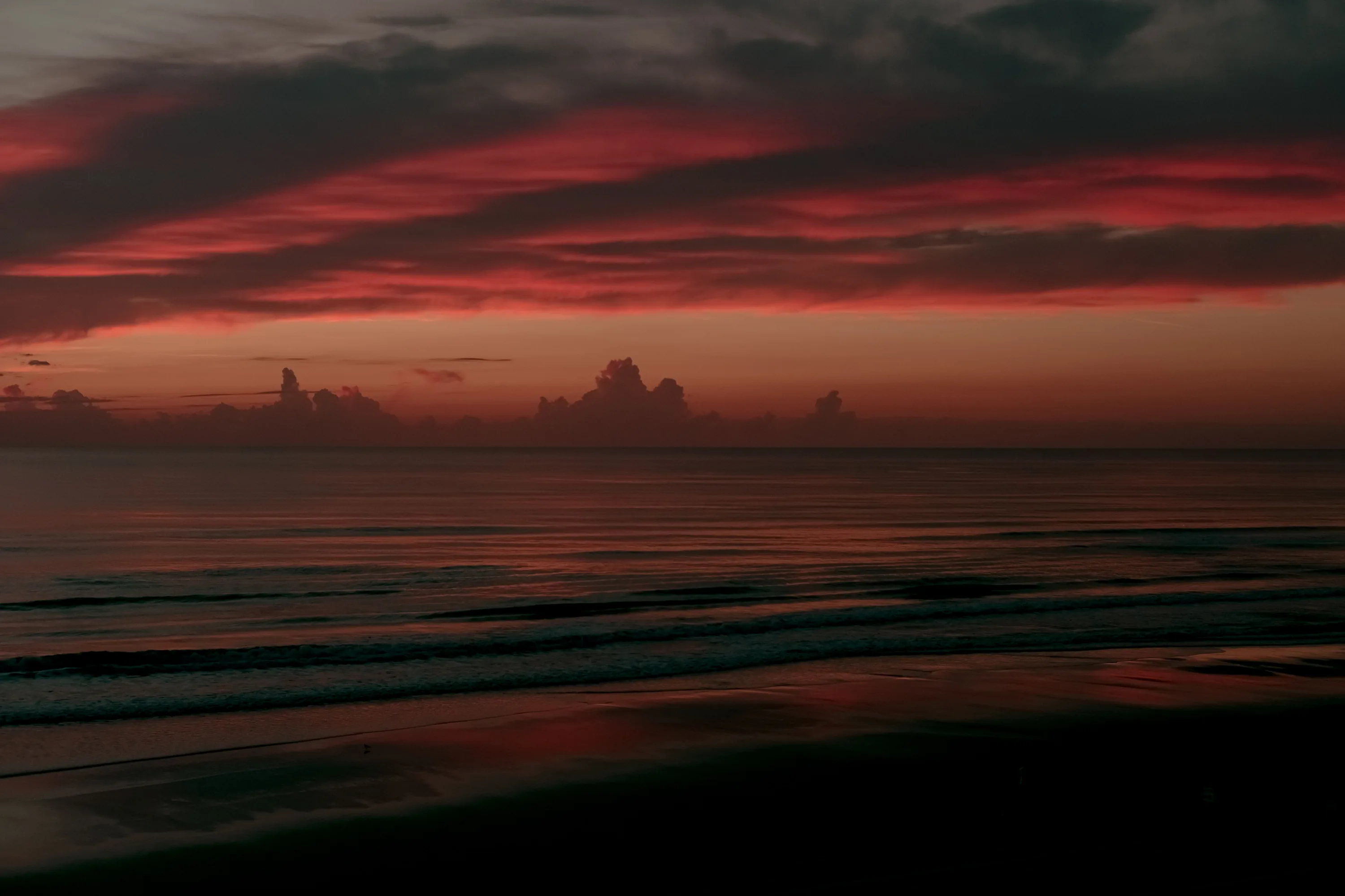 Streaks of maroon and pink cut across a nearly black sky and sea, the beach at the bottom fading to full shadow — a natural fit for OLED screens.