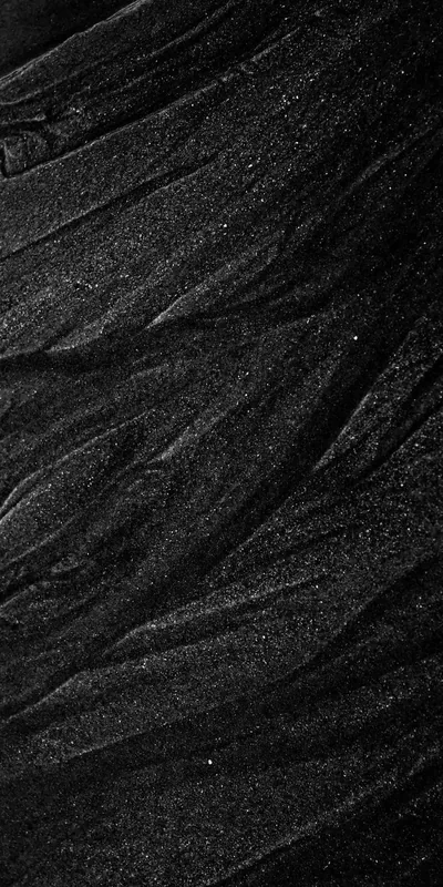 Fine ridges run diagonally across dark volcanic sand, lit from the side so each grain and ripple catches a sliver of light.
