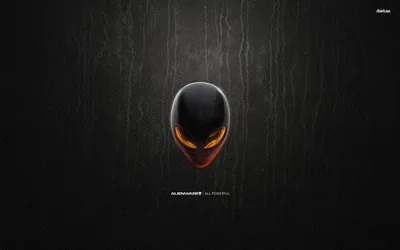 The alien head badge glows amber from within, mounted on a scratched dark wall, with the small Alienware wordmark centred beneath it.