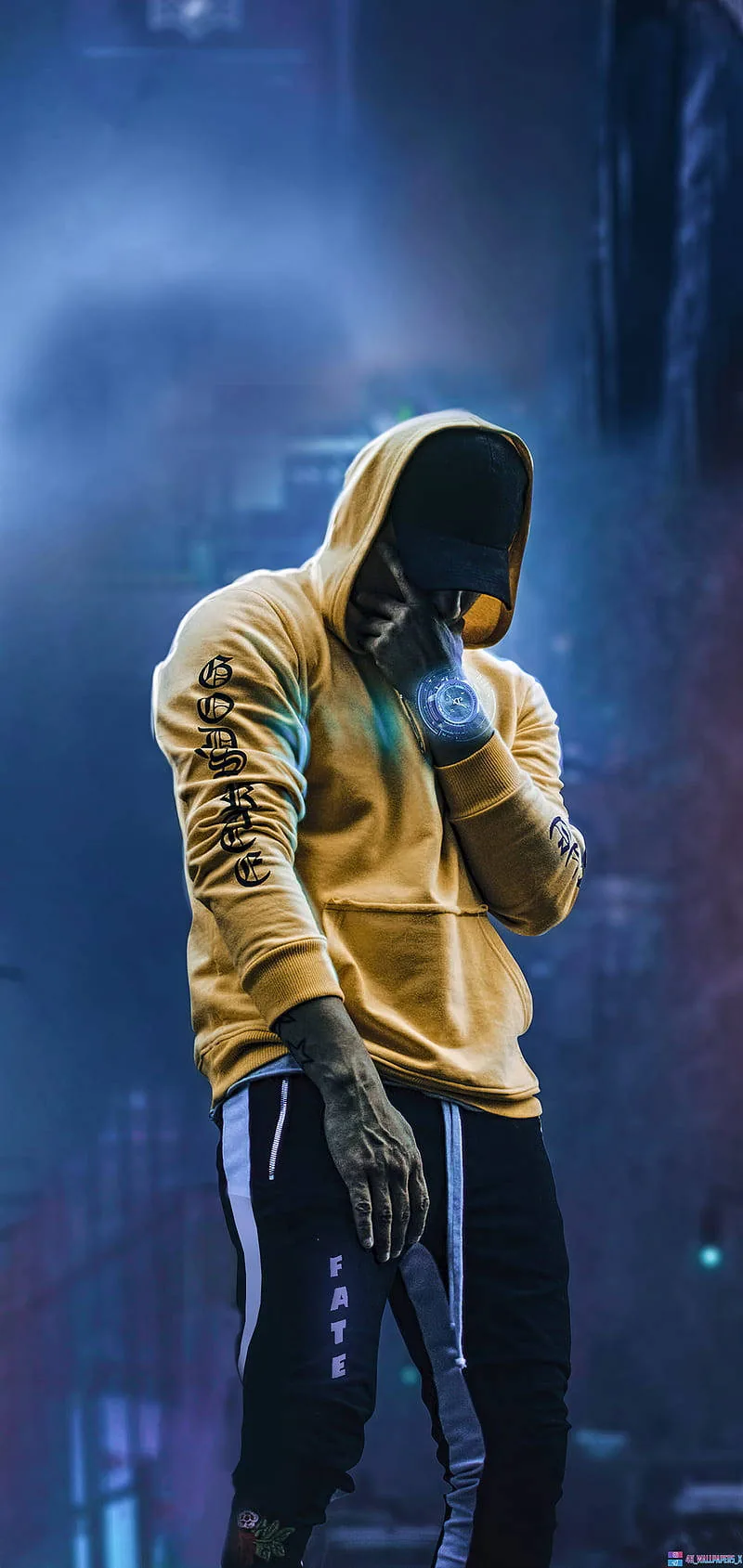 Head down in a mustard hoodie and a printed face mask, standing in front of a blurred blue neon street at night.