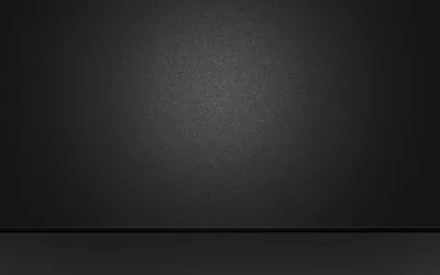 An empty studio wall in charcoal meets a darker floor along a straight seam, with a soft grainy pool of light at the centre and black corners.
