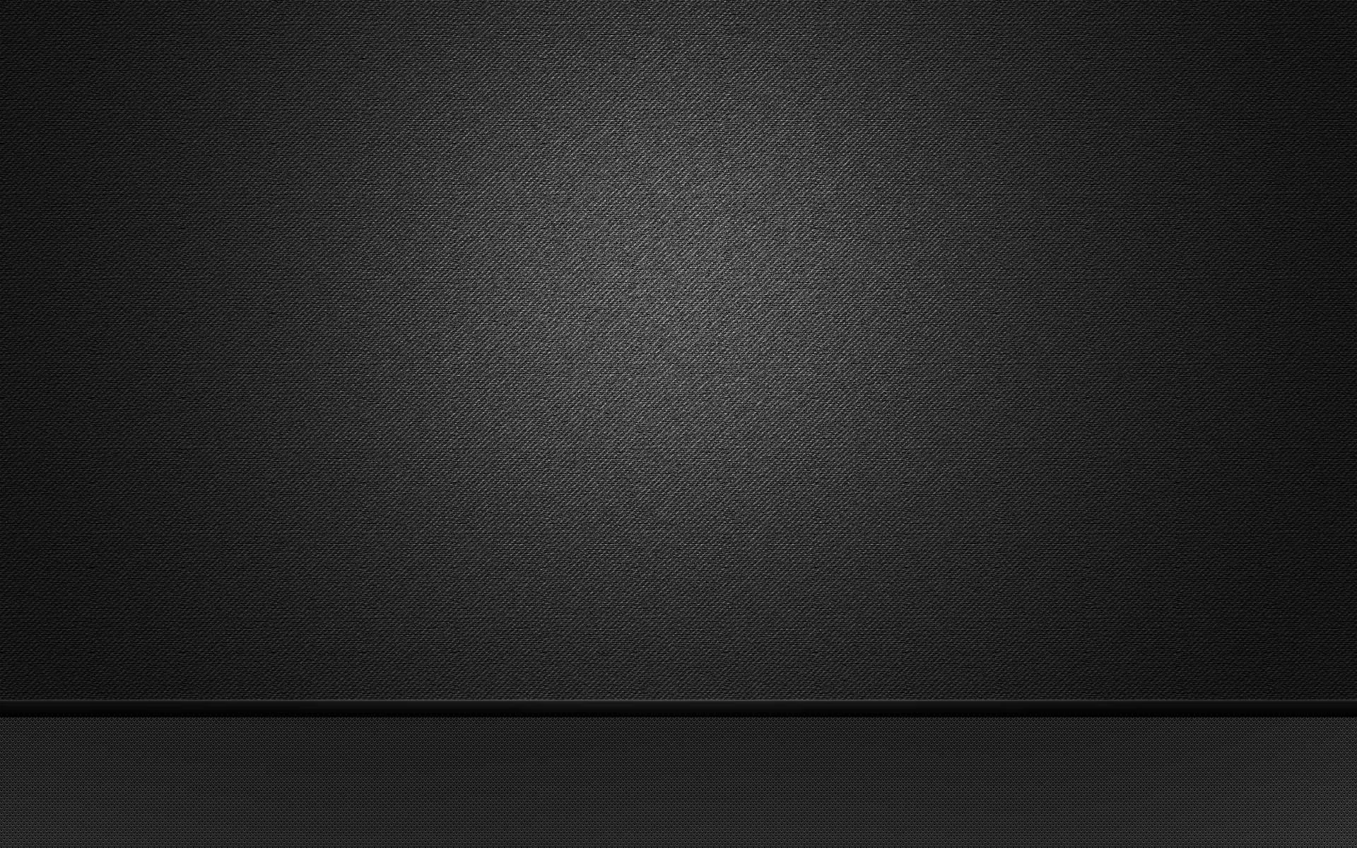 An empty studio wall in charcoal meets a darker floor along a straight seam, with a soft grainy pool of light at the centre and black corners.