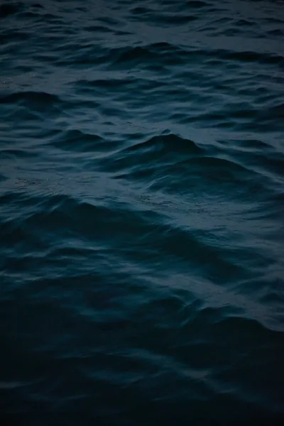 Low swells of deep teal water fill the whole vertical frame, the last light of dusk picking out pale crests on a few of the ridges.