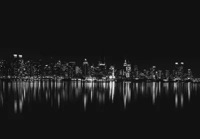 A dense skyline burns white against black sky, every tower repeating in the flat water across the foreground.