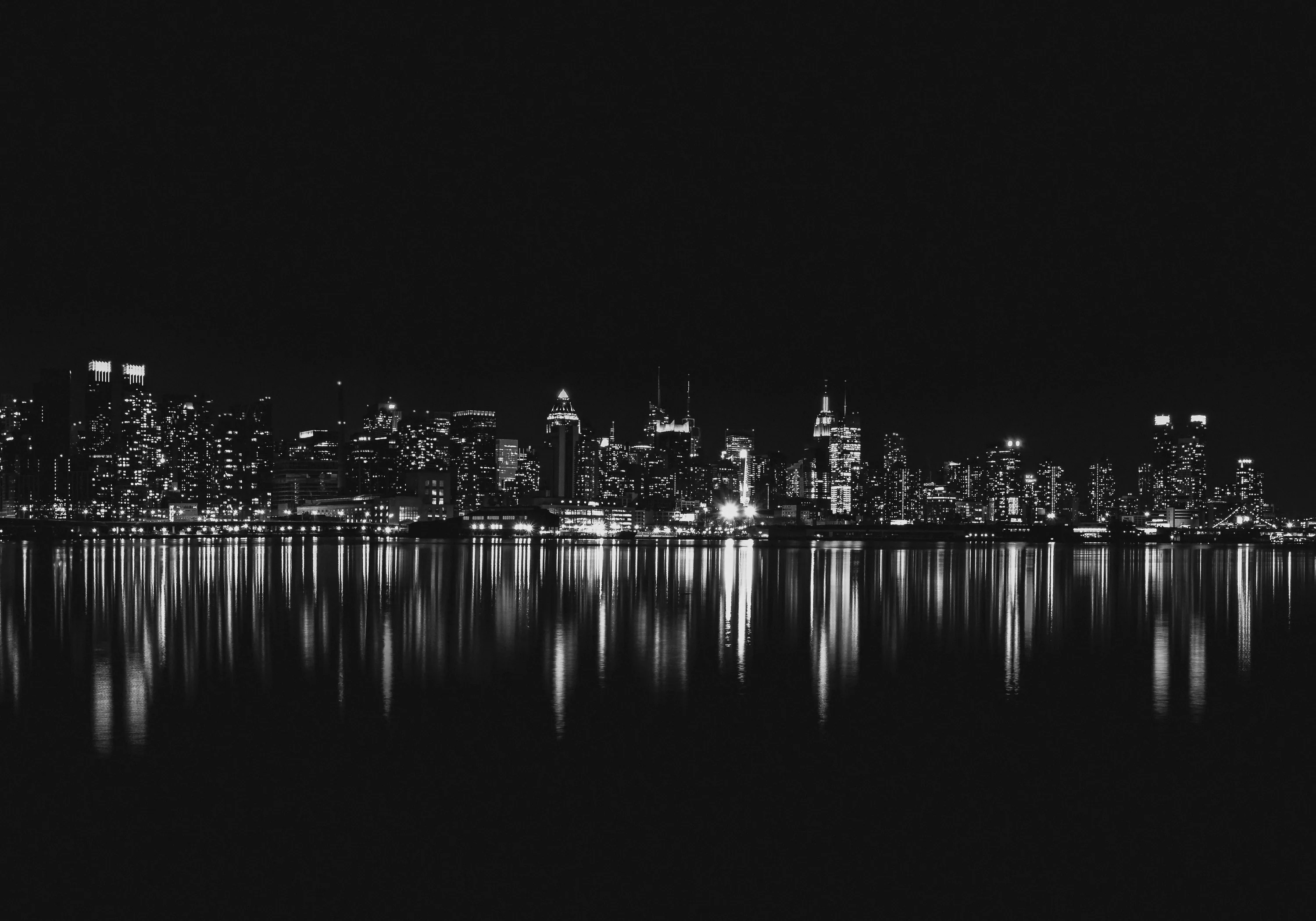 Manhattan towers glow in a thin band of monochrome light, the whole city mirrored in still black water below with empty sky above.