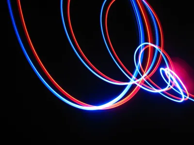 Long-exposure red and blue light loops cross a pure black frame, a pink flare at the right edge — mostly true black for OLED battery savings.