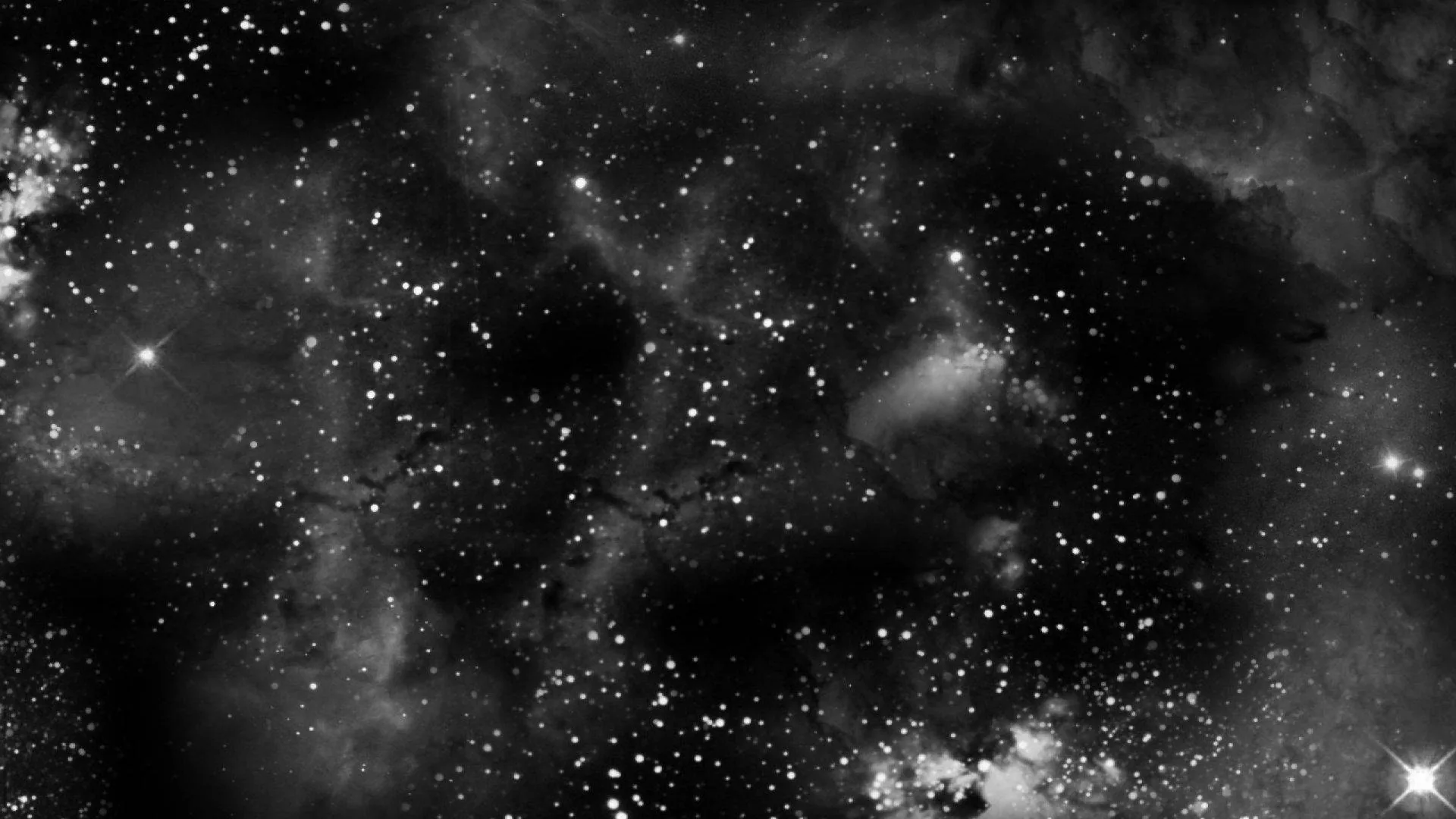 Curls of grey gas rise behind clusters of white stars in full monochrome, the brightest knot sitting toward the lower left.